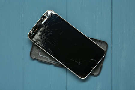 Damaged smartphone on light blue wooden table, top view. Device repairing