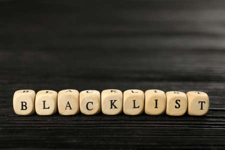 Cubes with word Blacklist on black wooden table, closeup
