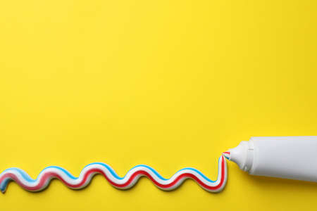Blank tube with squeezed out toothpaste on yellow background, flat lay. Space for textの写真素材