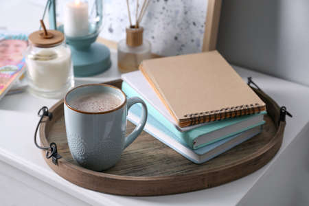Wooden tray with books and cup of coffee on white table indoorsの写真素材