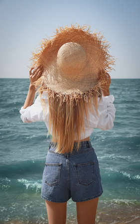 Young woman with straw hat near sea on sunny day in summer, back viewの写真素材