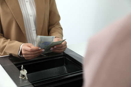 Cashier with money at currency department window in bank, closeup