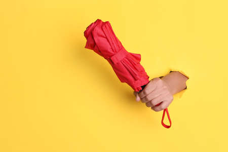 Woman holding red umbrella through hole in yellow paper, closeup. Space for textの写真素材