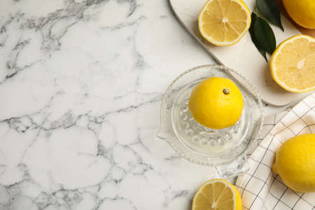 Glass squeezer and fresh lemons on white marble table, flat lay. Space for textの写真素材
