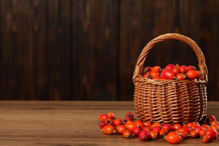 Ripe rose hip berries with wicker basket on wooden table. Space for textの写真素材