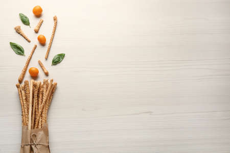 Delicious grissini sticks, basil leaves and yellow tomatoes on white wooden table, flat lay. Space for textの写真素材