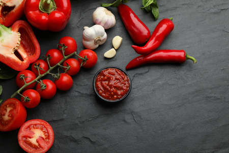 Delicious adjika sauce in bowl and ingredients on black table, flat layの写真素材