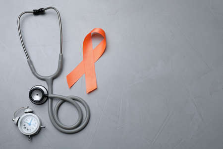 Orange ribbon, stethoscope and alarm clock on light gray table, flat lay with space for text. Multiple sclerosis awarenessの写真素材