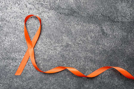 Orange ribbon on gray table, top view with space for text. Multiple sclerosis awareness