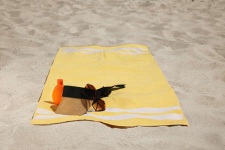 Beach towel with visor cap, sunglasses and sunscreen on sandの写真素材