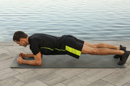 Sporty man doing plank exercise on mat outdoors