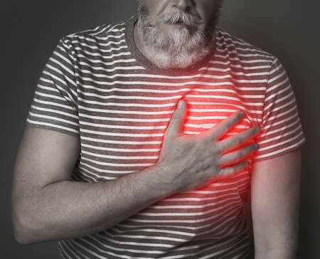 Mature man having heart attack on dark background, closeup viewの写真素材
