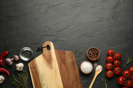 Flat lay composition with wooden cutting board and ingredients on black table, space for text....