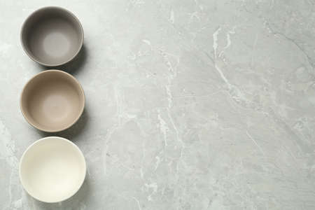 Stylish empty ceramic bowls on gray table, flat lay and space for text. Cooking utensils