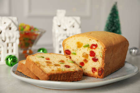 Delicious cake with candied fruits and Christmas decor on light gray table