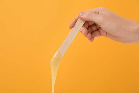 Woman holding spatula with hot depilatory wax on yellow background, closeupの写真素材