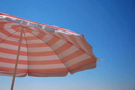 Red and white striped beach umbrella against blue sky, space for text