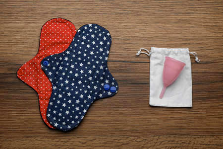 Reusable cloth pads and menstrual cup on wooden table, flat layの写真素材