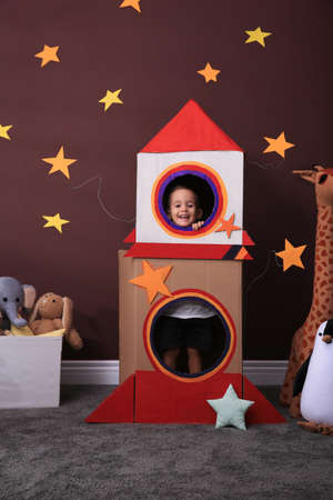 Cute little boy playing with cardboard rocket and toys at home. Child's room interiorの写真素材