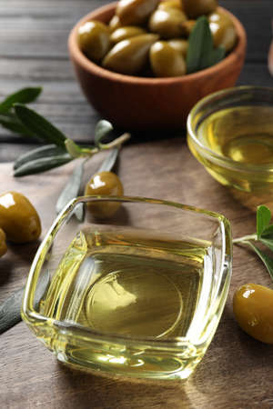 Glass bowls of oil, ripe olives and green leaves on wooden table