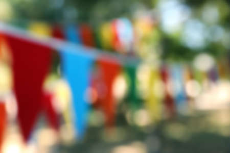 Blurred view of colorful bunting flags in park. Party decor
