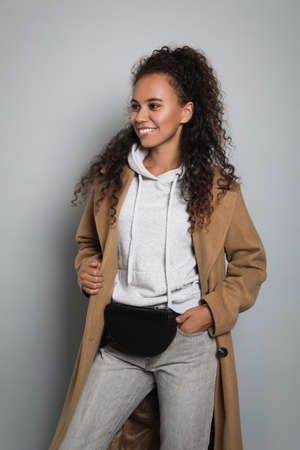Beautiful African American woman with stylish waist bag on gray backgroundの写真素材