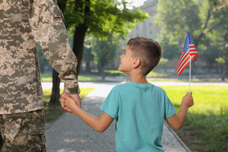 Soldier and his little son with American flag outdoors, back view. Veterans Day in USAの写真素材