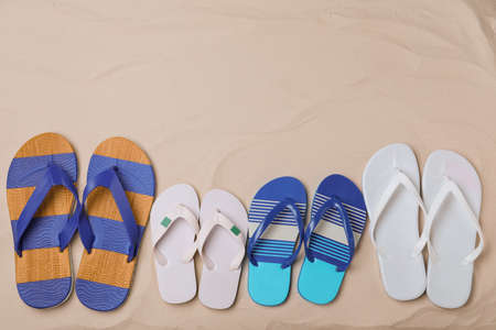 Different bright flip flops on sand, flat lay. Space for textの写真素材