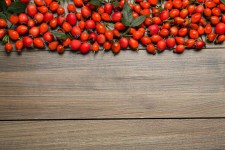 Ripe rose hip berries with green leaves on wooden table, flat lay. Space for textの写真素材