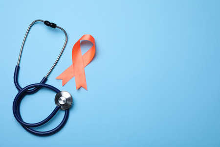 Orange ribbon and stethoscope on light blue background, flat lay with space for text. Multiple...