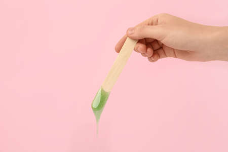Woman holding spatula with hot depilatory wax on pink background, closeupの写真素材