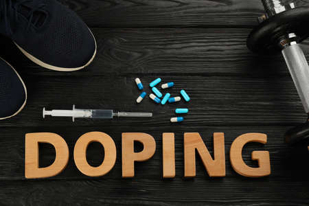 Word Doping, sport shoes, dumbbell and drugs on black wooden background, flat layの写真素材
