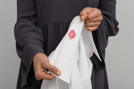 Woman holding her husband's shirt with lipstick kiss mark against white background, closeup
