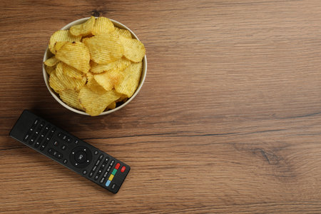 Modern tv remote control and chips on wooden table, flat lay. Space for textの写真素材