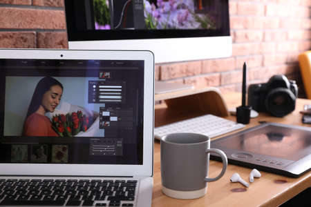 Modern retoucher's workplace with different digital devices on wooden table near red brick wallの写真素材