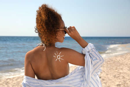 Beautiful African American woman with sun protection cream on shoulder at beach, back view