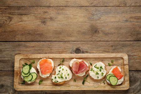 Delicious sandwiches with cream cheese and other ingredients on wooden table, top view. Space for...