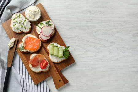 Toasted bread with cream cheese and different toppings on white wooden table, flat lay. Space for textの写真素材