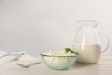 Delicious fresh cottage cheese with basil and milk on white wooden table. Space for textの写真素材