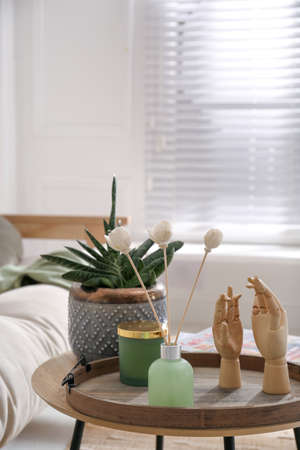 Wooden tray with air reed freshener, plant and mannequin hands on table in living roomの写真素材