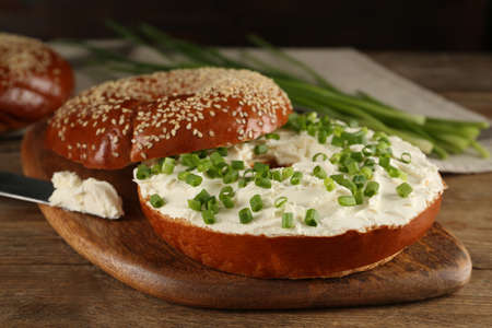 Delicious bagel with cream cheese and green onion on wooden table, closeupの写真素材