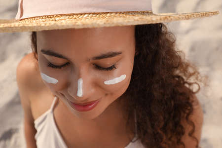 Beautiful African American woman with sun protection cream on face at sandy beach, closeupの写真素材