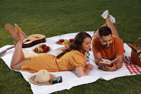 Happy young couple reading book on picnic plaid outdoorsの写真素材