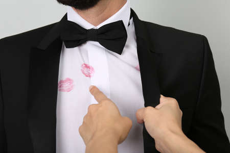 Woman pointing at lipstick kiss marks on her husband's shirt against white background, closeup