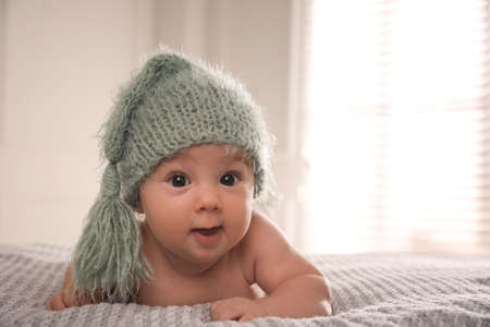Cute little baby wearing knitted hat on bed at home, space for text