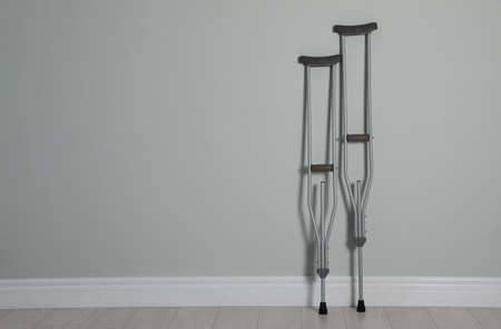 Pair of axillary crutches near light gray wall. Space for textの写真素材
