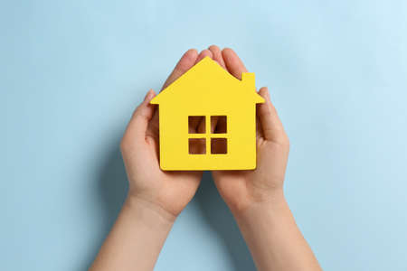 Woman holding house figure on light blue background, top viewの写真素材
