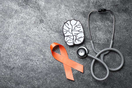 Orange ribbon, stethoscope and paper brain cutout on gray table, flat lay with space for text....