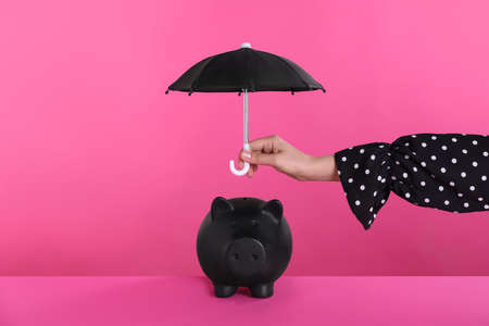 Woman holding small umbrella over piggy bank on pink background, closeupの写真素材