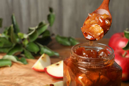 Spoon with tasty apple jam over glass jar at table, closeup. Space for text